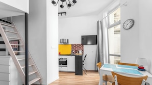 A modern kitchen with a yellow backsplash, a dining area with a wooden table and chairs, and a staircase leading to another level. - Morsztynowska Studio with Mezzanine (Kraków)