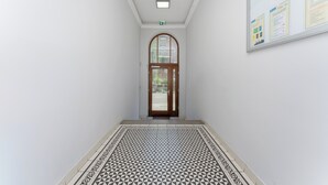 A hallway with a patterned floor, a wooden door at the end, and a bulletin board on the wall. - Morsztynowska Studio with Mezzanine (Kraków)