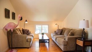 A living room with two sofas, a coffee table, a lamp, and a flamingo statue. - Cozy 3-Bedroom Beach Cottage (Turkey Point)