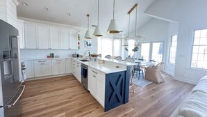 Une cuisine spacieuse avec des meubles blancs, un îlot central et des luminaires suspendus.