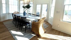 Un vaste espace dédié à la salle à manger, avec une grande table en bois, des chaises noires et un luminaire suspendu.