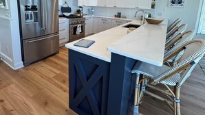 Une cuisine moderne avec des meubles blancs, des appareils en acier inoxydable et un grand îlot central doté de tabourets.