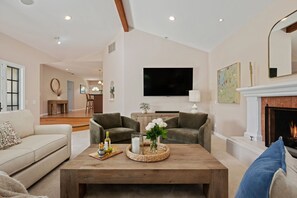 Uma sala de estar com lareira, televisão e um espaço de refeições ao fundo.