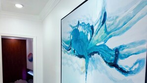 Een gang met een groot abstract schilderij aan de muur, een deur naar een slaapkamer, en een marmeren vloer.