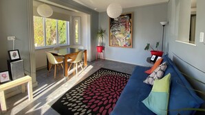 Un salon moderne comprenant un coin repas, de grandes fenêtres, un canapé bleu et un tableau abstrait aux couleurs vives.