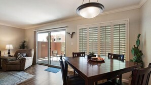 Un espace repas comprenant une table et des chaises en bois, un lustre et une porte-fenêtre coulissante donnant sur une terrasse extérieure.