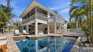 Une maison à deux étages avec une piscine, un espace salon extérieur et une clôture blanche.