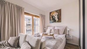 Une chambre avec un grand lit, une table de chevet, une fenêtre avec des rideaux et un tableau au mur.