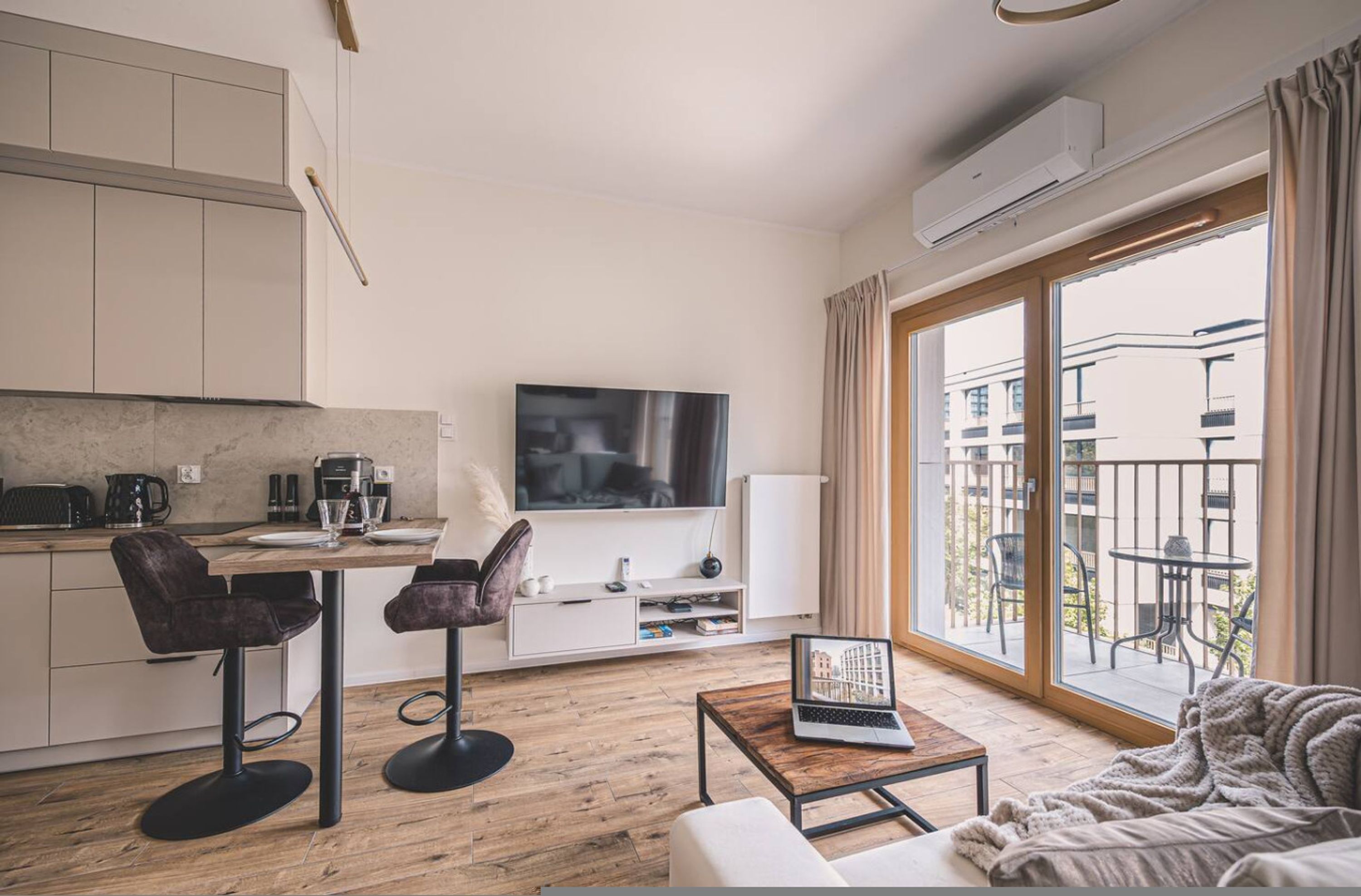 Una sala de estar moderna con un televisor de pantalla plana, un sofá, una mesa de centro y un balcón con mobiliario exterior.