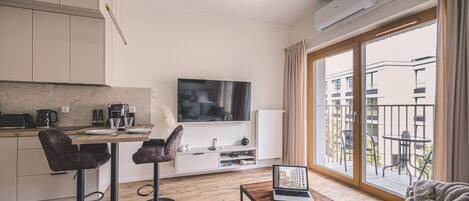 Una sala de estar moderna con un televisor de pantalla plana, un sofá, una mesa de centro y un balcón con mobiliario exterior.