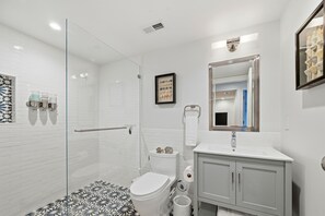 Une salle de bain moderne avec une douche à parois de verre, des toilettes, un lavabo avec un miroir et un carrelage décoratif.