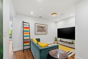 Un salon moderne avec un canapé turquoise, des coussins jaunes, un téléviseur noir et un porte-serviettes rayé aux couleurs vives.
