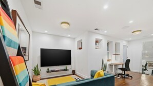 A modern living room with a flat-screen TV, a sofa, a desk, and a chair.