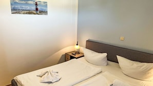 A hotel room with two beds, a nightstand with a lamp, and a picture of a lighthouse on the wall. - Lovely apartment for 4 people with WIFI, TV and balcony (Wolgast)