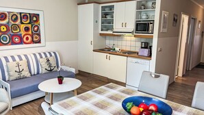 A compact living space with a kitchenette, a dining area with a table and chairs, a sofa with striped cushions, and a colorful abstract painting on the wall. - Lovely apartment for 4 people with WIFI, TV and balcony (Wolgast)