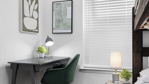 A modern bedroom with a dark grey desk, a green chair, a bedside table with a lamp, and a window with blinds. - Prime Location Zilker Park & SoCo Chic (Austin)