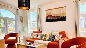 Ein modernes Wohnzimmer mit Sofa, zwei Sesseln, einem Couchtisch und einem großen Fenster mit Vorhängen.