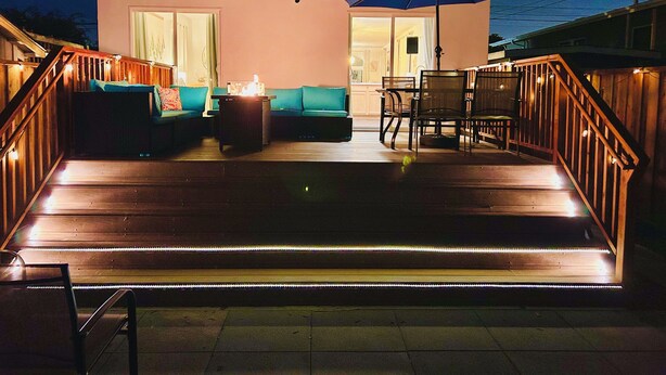 Eine moderne Außenpatio mit Holzboden, einer Couch, einem Tisch und Stühlen.