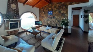 Amplia sala de estar con pared de piedra, chimenea, televisor y una cómoda disposición de asientos.