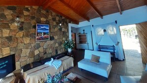 Una sala de estar acogedora con una pared de piedra, vigas de madera en el techo, un sofá blanco y un televisor.