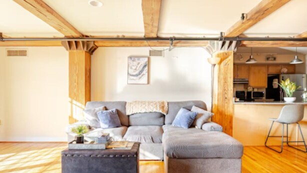 A modern living room with a grey sectional sofa, a dark ottoman, and a wooden floor.