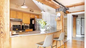 A kitchen with wooden cabinets, a stainless steel refrigerator, a sink, and two bar stools.