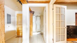 A hallway with a wooden floor, a tiled shower area, and a door leading to a room with a dark-colored dresser.