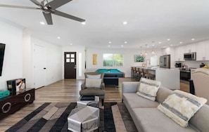A modern living room with a pool table, a sofa, and a dining area.