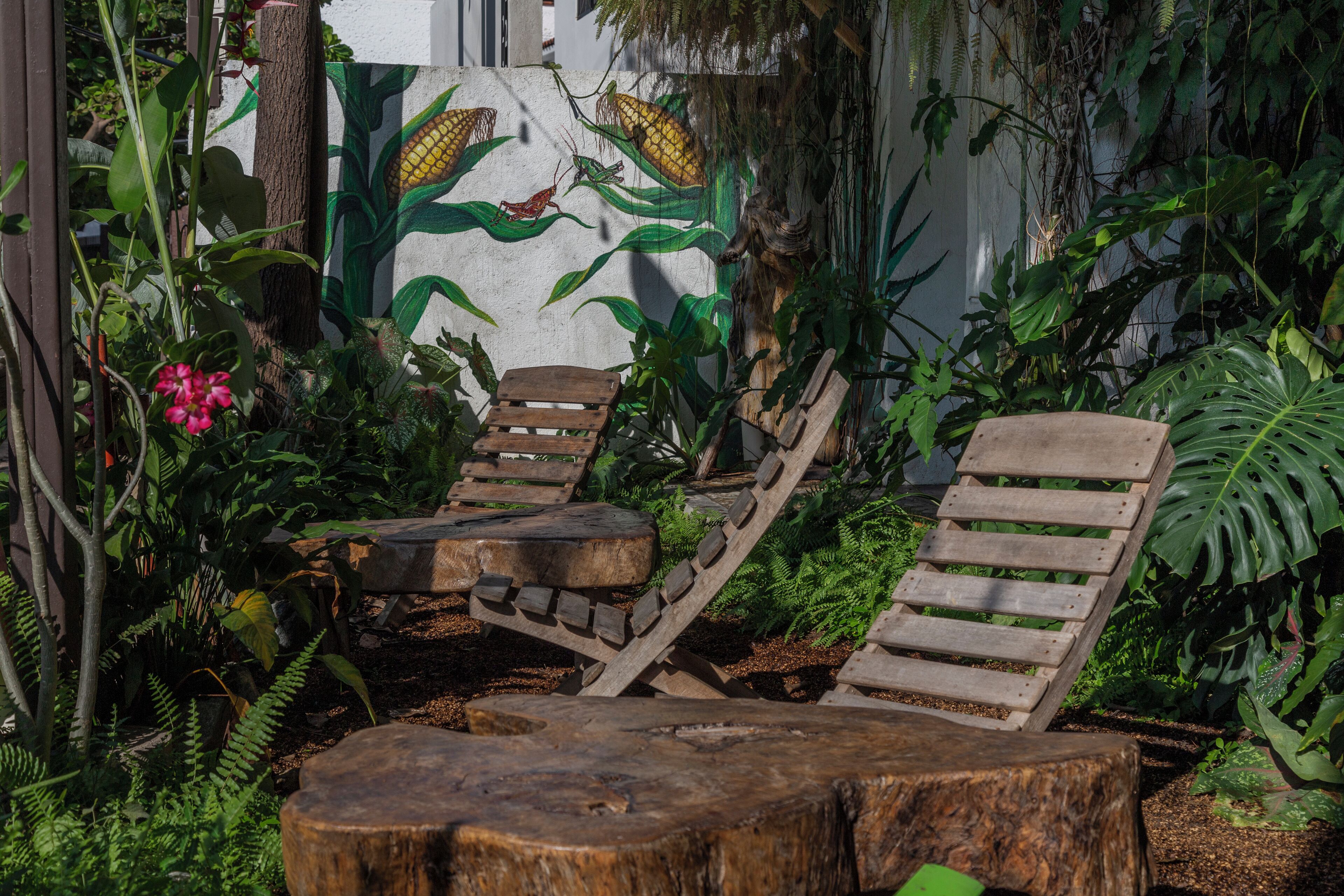 Two wooden lounge chairs in a garden with a mural of corn and a frog.