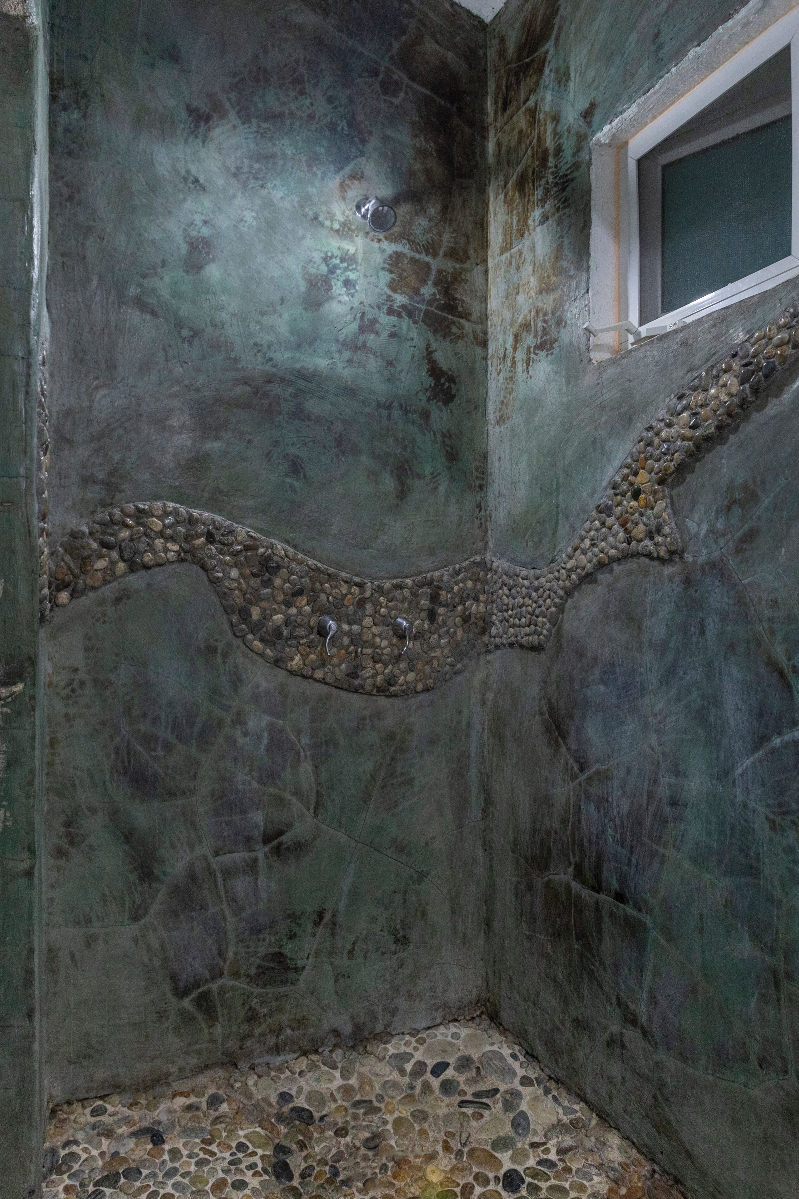 Ein Zimmer mit strukturierter Wand, einem kleinen Fenster und einem Boden mit Kieselsteinen.