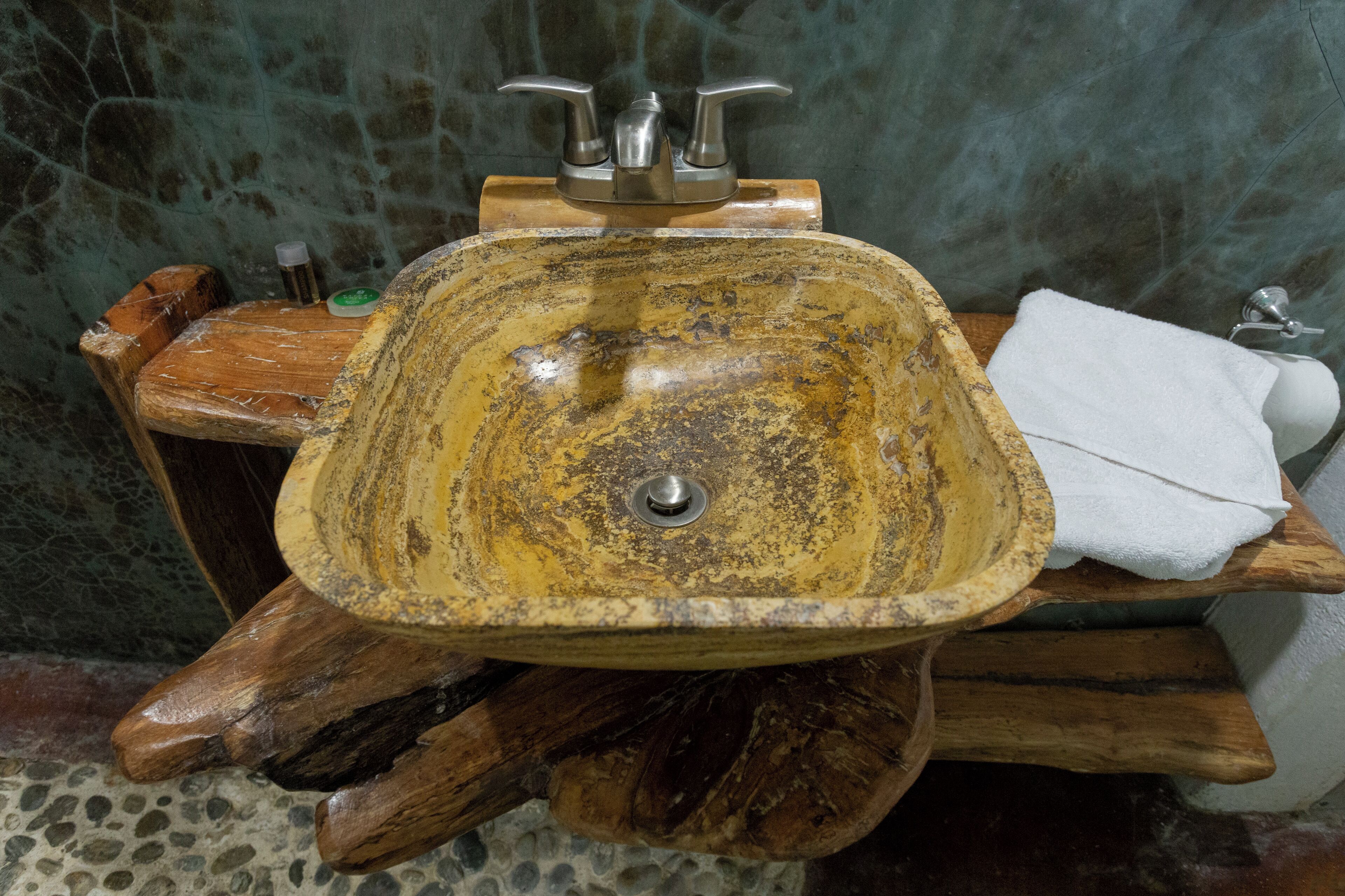 Une salle de bain rustique avec un grand lavabo en céramique de couleur jaune-brun, de forme ovale, posé sur un support en bois.