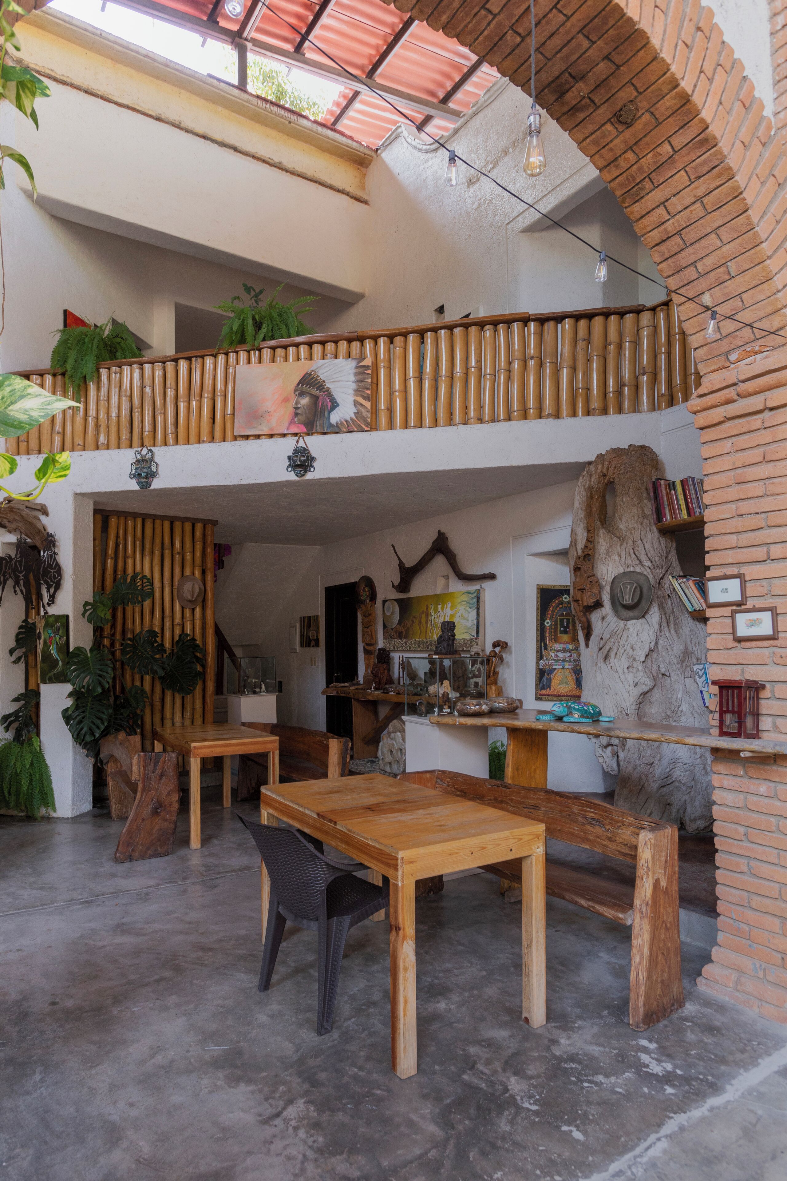 A spacious interior with a wooden table and chairs, a balcony with plants, and a brick wall with a tree trunk sculpture.