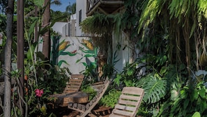 Un rigoglioso giardino con mobili in legno, tra cui una panchina e un tavolo, circondato da fitta vegetazione e una struttura in bambù.