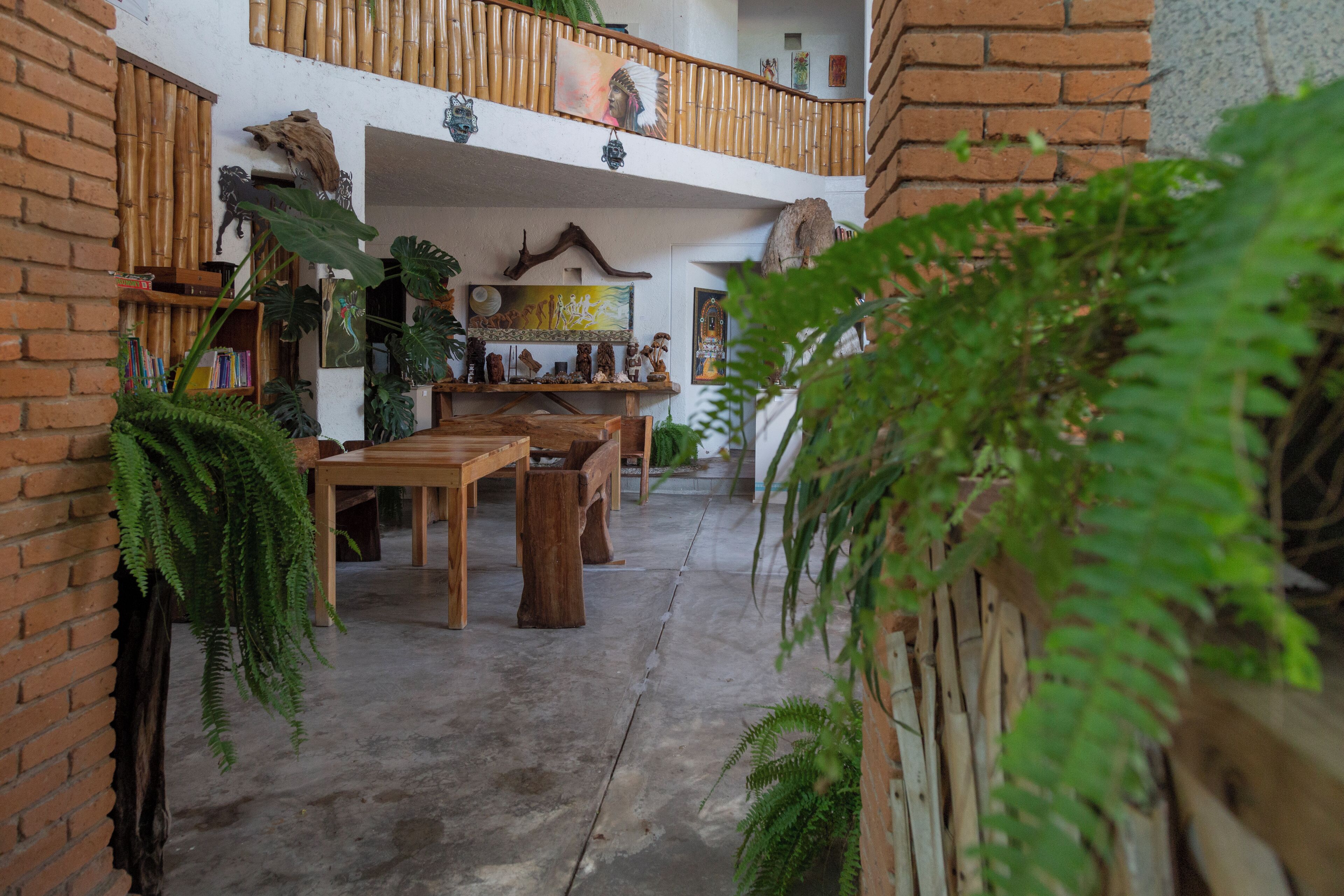 A spacious indoor area with a high ceiling, featuring a wooden balcony, a dining area with tables and chairs, and various decorative items and plants.
