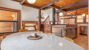 A modern kitchen with wooden beams, a round marble table, and built-in appliances.