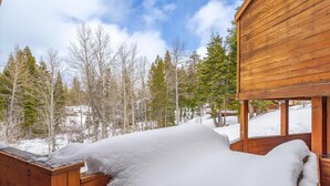 A wooden cabin with a snow-covered deck and a view of a forested area.