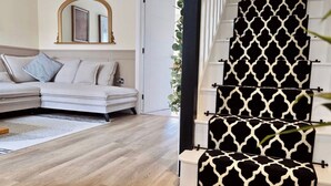 Una sala moderna con un sofá modular, piso de madera y una escalera con peldaños estampados.