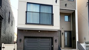 A modern two-story residential building with a garage, a staircase, and a small balcony. - Luxury 3BR Retreat Near NYC (Newark)