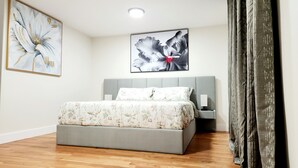 A modern bedroom with a grey upholstered bed, floral bedding, and two framed artworks on the walls. - Luxury 3BR Retreat Near NYC (Newark)