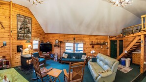 A log cabin interior with a fireplace, green sofa, rocking chair, and a wooden staircase. - Secluded Woodland Retreat Surrounded by Forest Views & Wildlife (Mill Hall)