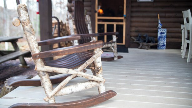 A rustic wooden rocking chair on a wooden deck with a cabin in the background. - Secluded Woodland Retreat Surrounded by Forest Views & Wildlife (Mill Hall)