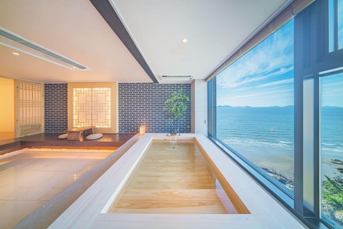Un spa moderno con suelo de madera, un ventanal grande con vistas al mar y una pared de ladrillo con un diseño geométrico.