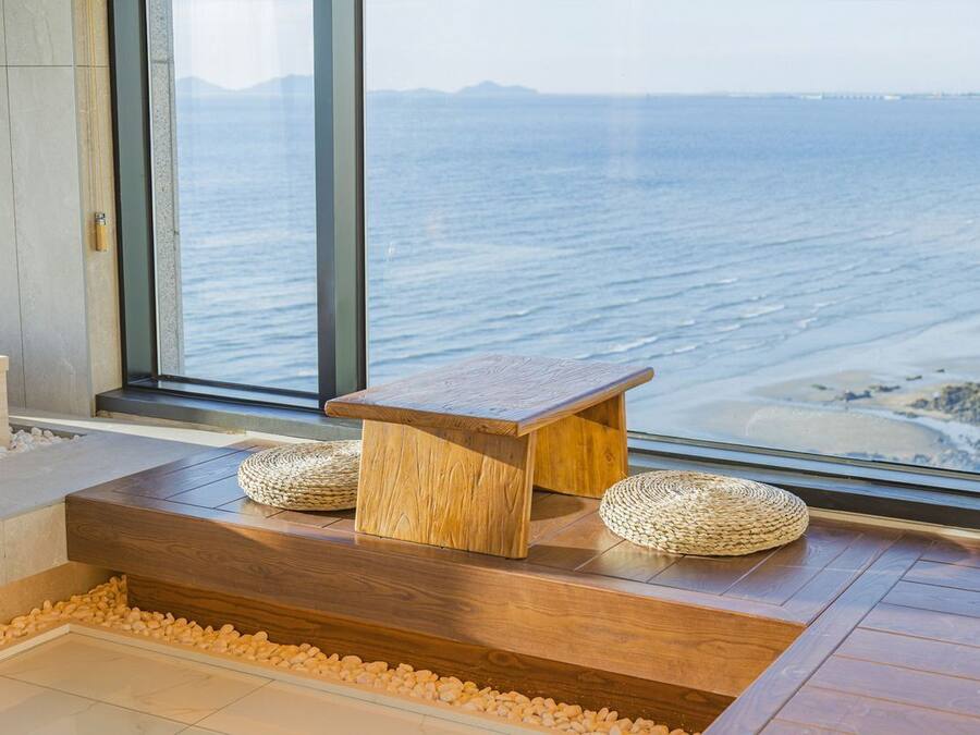 A wooden bench with woven baskets, a stone ledge, and a view of the ocean through a large window.