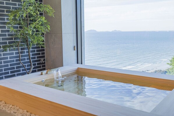 A modern spa area with a wooden tub, a brick wall, and a view of the ocean.