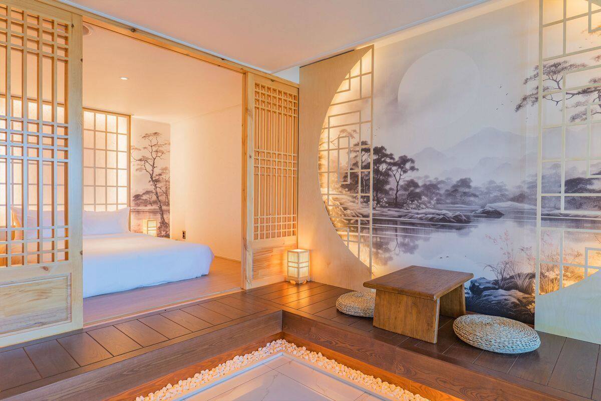 Una habitación de estilo japonés tradicional con suelo de tatami, una cama de madera baja, una puerta corredera y un mural con un paisaje sereno.