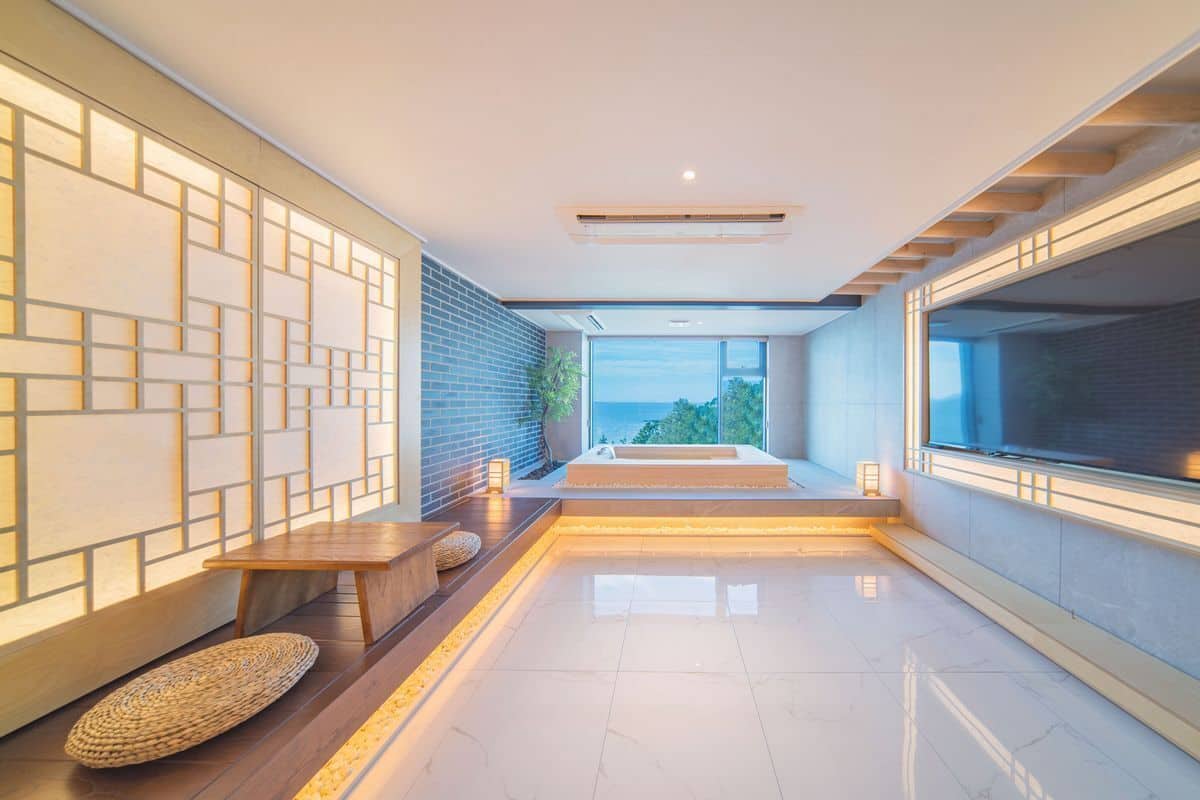 Un interior moderno con un banco de madera, una mesita y vistas al exterior a través de amplios ventanales.