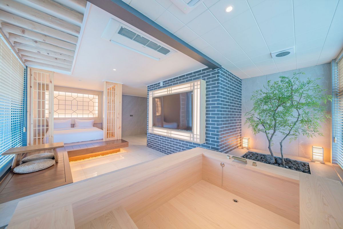 A modern spa room with a wooden floor, a seating area, a large mirror, and a small tree.