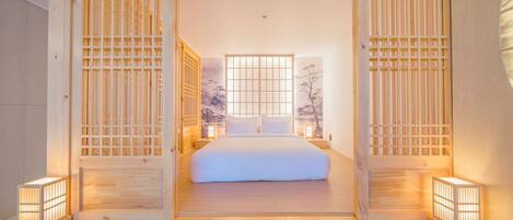 Une chambre de style japonais traditionnel, dotée d’un grand lit, de portes coulissantes et offrant une vue sur un arbre par la fenêtre.
