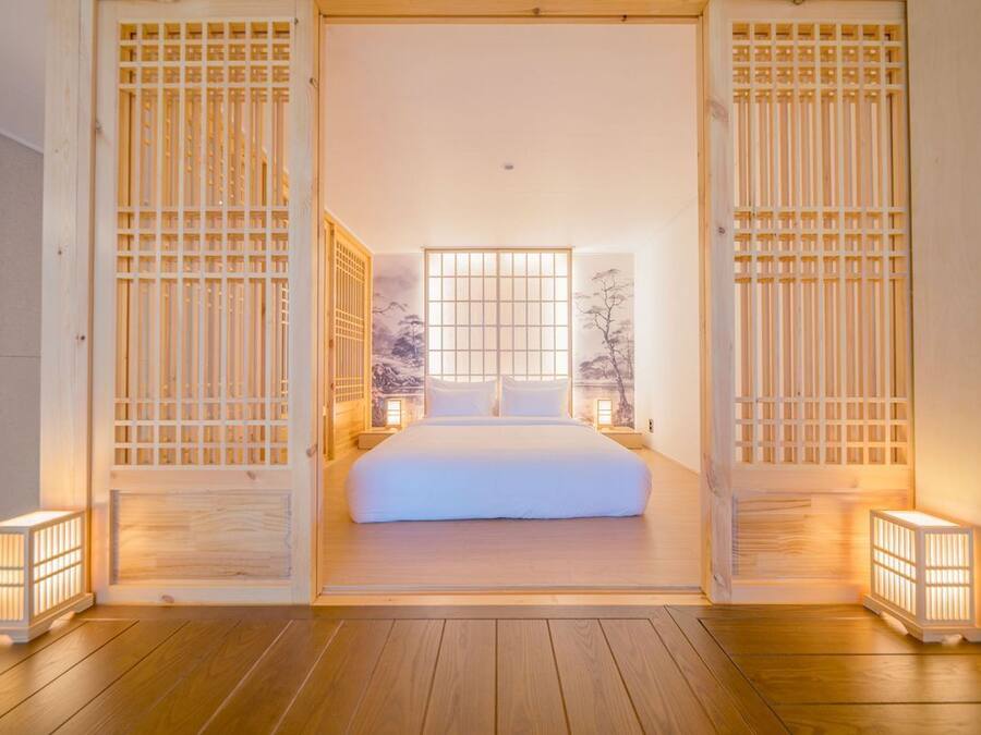 A traditional Japanese-style bedroom with a large bed, sliding doors, and a view of a tree through a window.