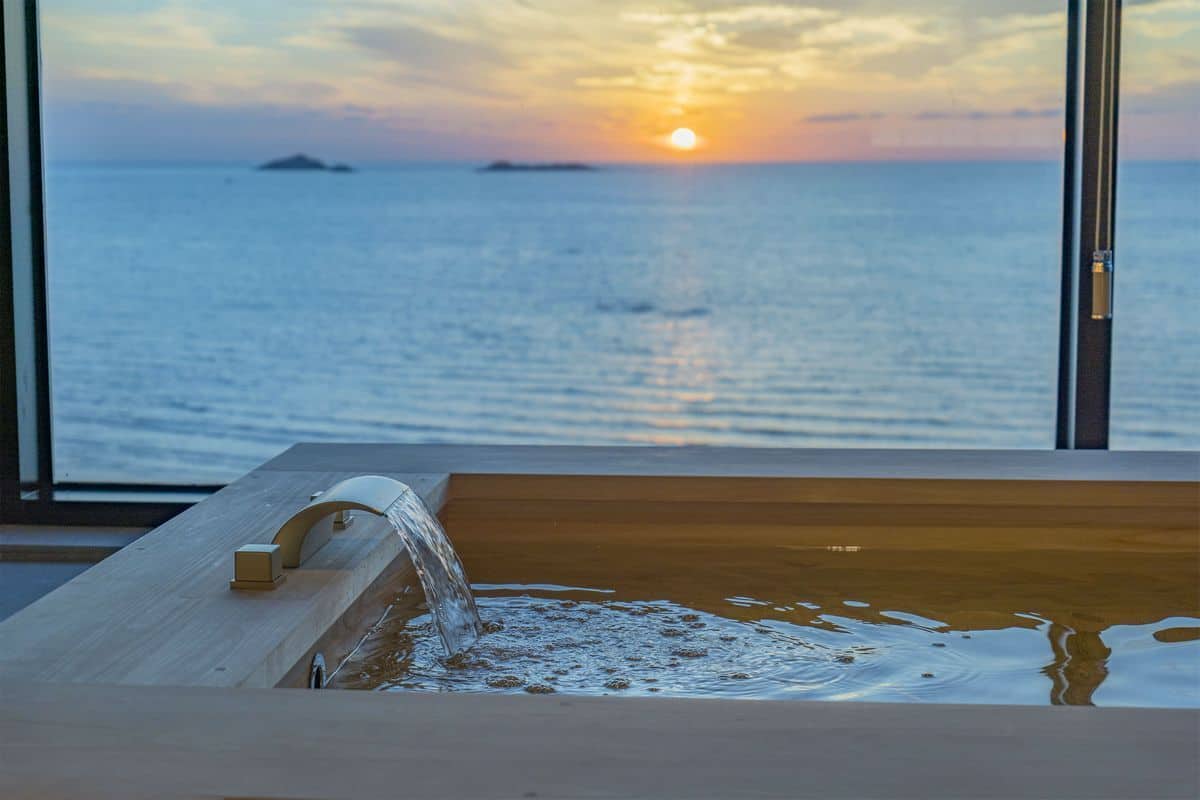 Una bañera con agua corriente, con vistas a un atardecer sobre el mar.